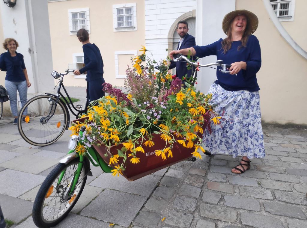 Frau mit Fahrrad / Lastenrad voller gelber Blumen